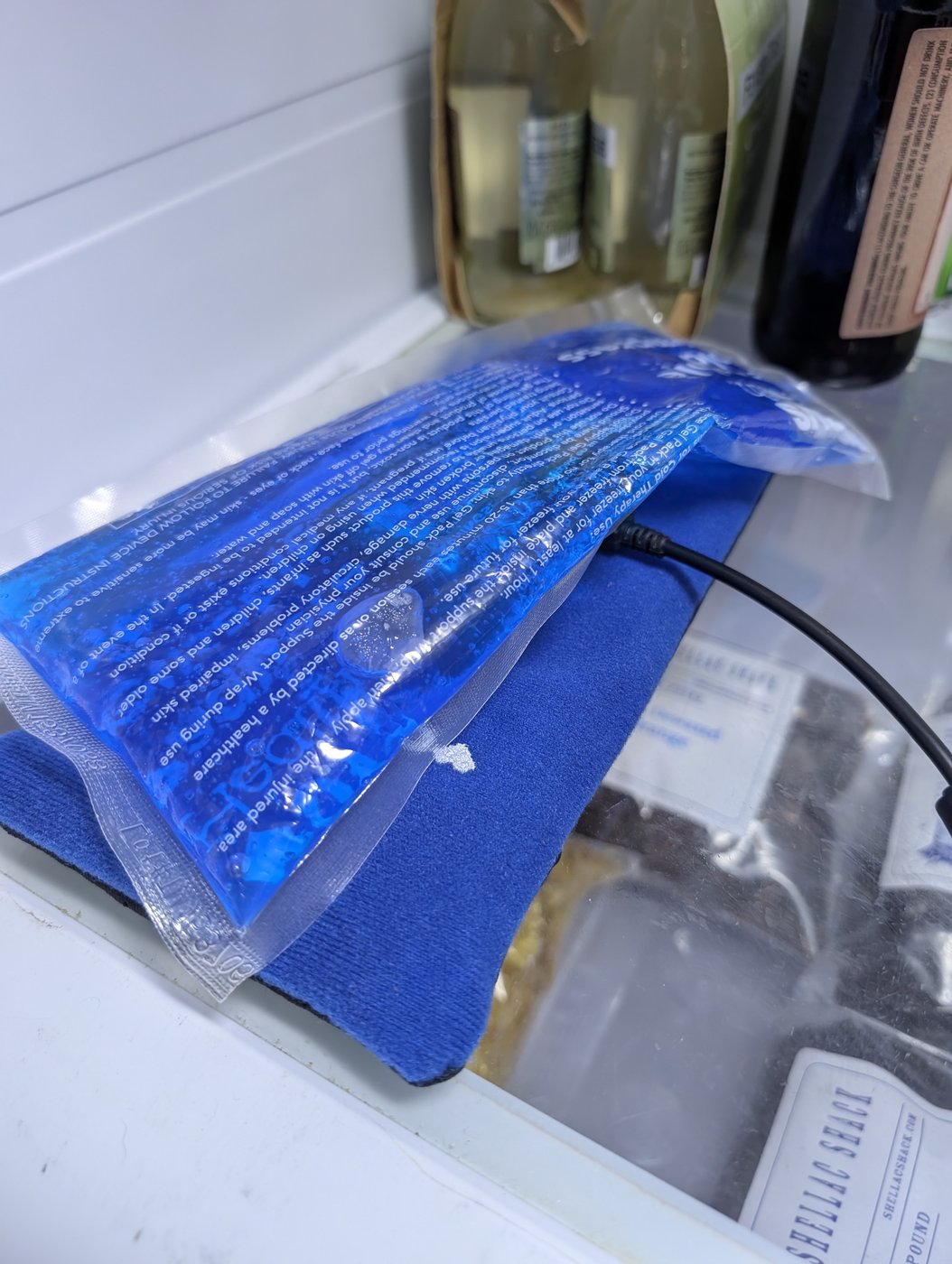 A second bare gel pack laid over the device, completing the sandwich; only the USB cable emerges.